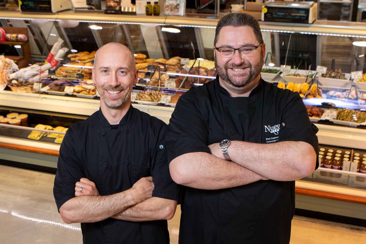 Two Nugget Markets chefs with arms folded in front of prepared foods case